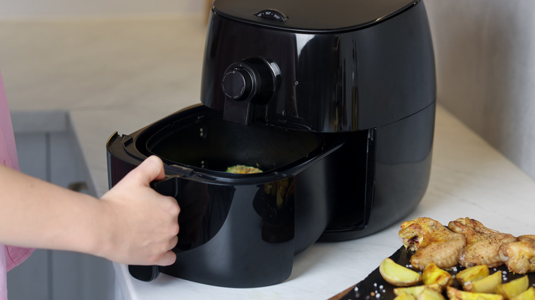 An airfryer on a counter with someone opening the cooking drawer