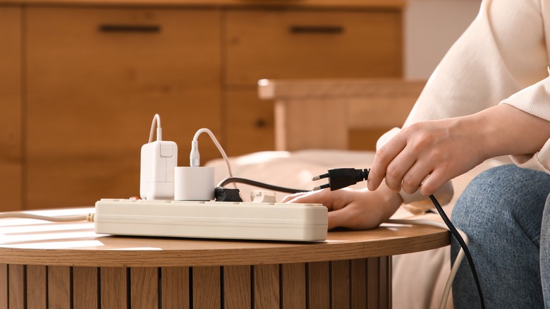 A woman next to a power strip removing one of the power cables from the device