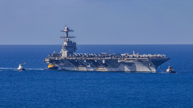 U.S.S. Gerald Ford aircraft carrier in the water with tugboats visible.
