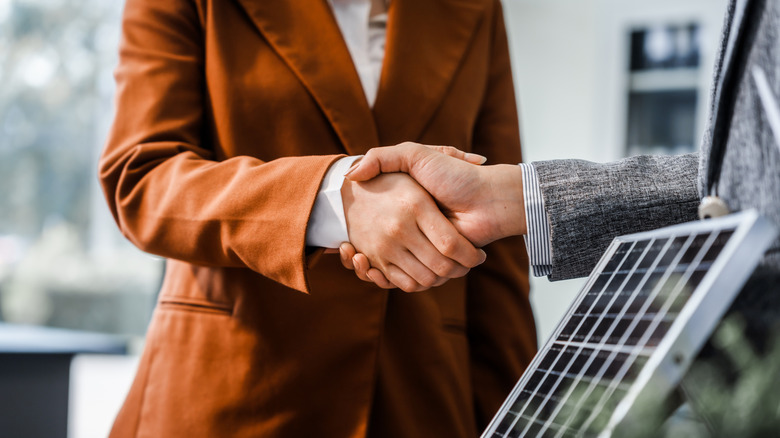Two people in suits shaking hands, making a business deal