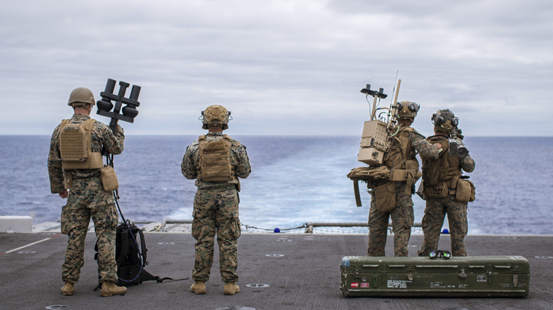 A group of marines stand aboard a naval vessel, staring out into the ocean as they prep their anti-drone defenes.
