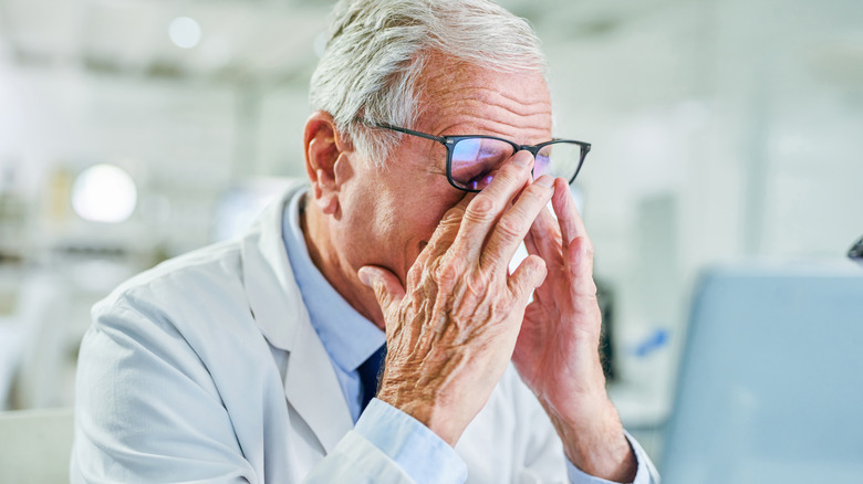 older male scientist, worried, hands in front of his face