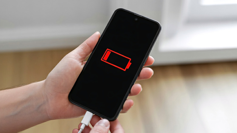 A person holding a phone plugged into a charger with the screen displaying an empty battery icon