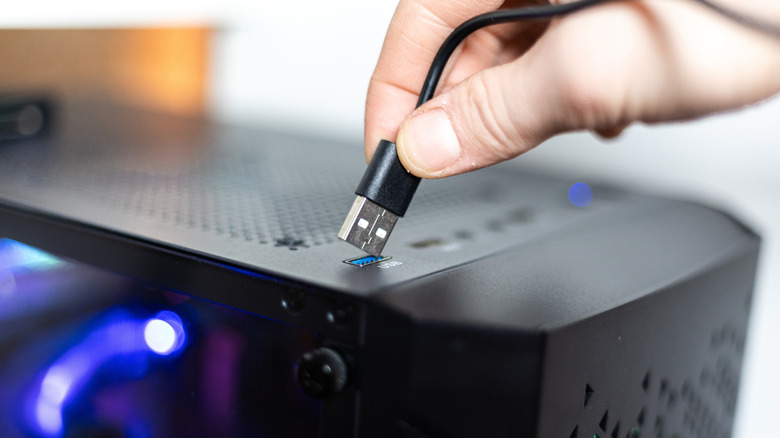 Someone connecting a USB cable to a port on the top of a desktop tower.