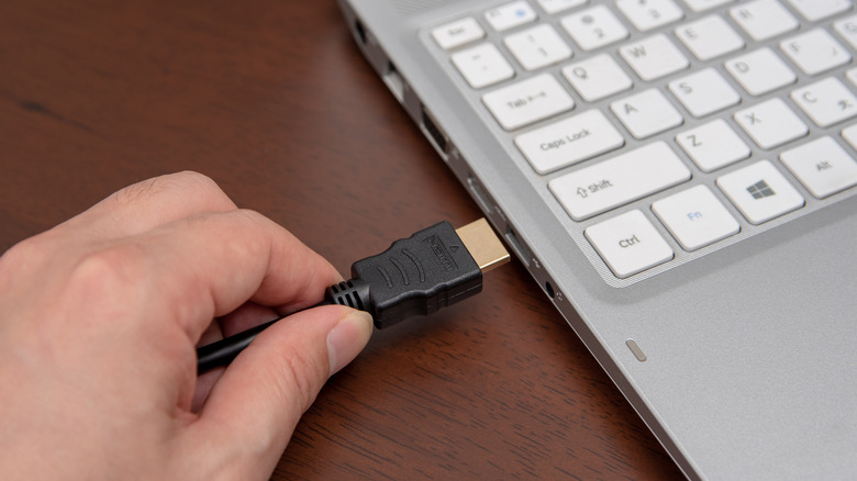 A person connecting a black HDMI cable into a laptop