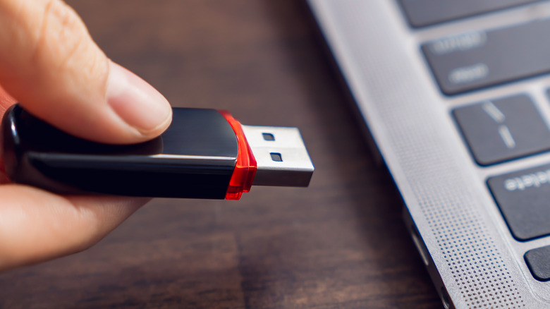 A close-up of a person about to connect a USB flash drive to a laptop.