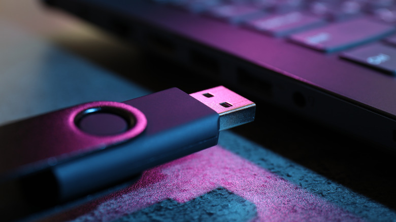 USB drive being plugged into the port on a side of a laptop with a purple glow.