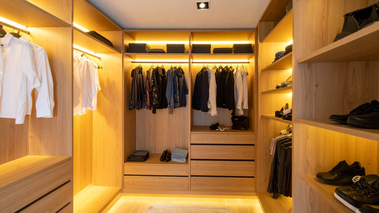 Well-organized walk-in closet with wooden shelving, clothes hanging, shoes, and warm LED lighting