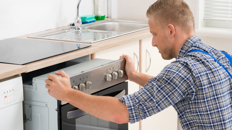Young repairman in overalls working on oven in kitchen
