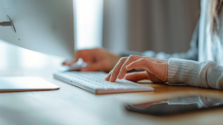 Close up of someone using a stylish wireless keyboard in an office setting.