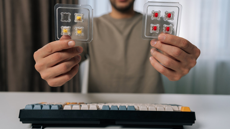 Someone holding up two different mechanical keyboard switches for comparison.