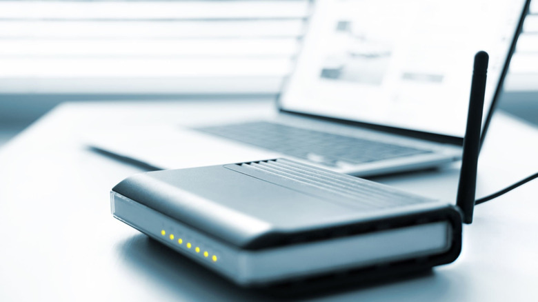 An internet wireless router on the desk, with a modern laptop in the background