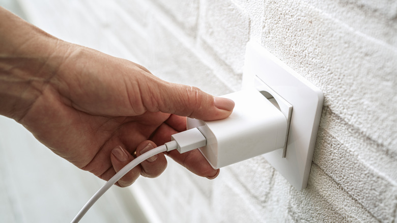 A hand plugging a charger into a wall outlet