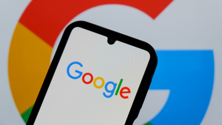 Google lettering displayed on on a smartphone with the Google logo in the background.