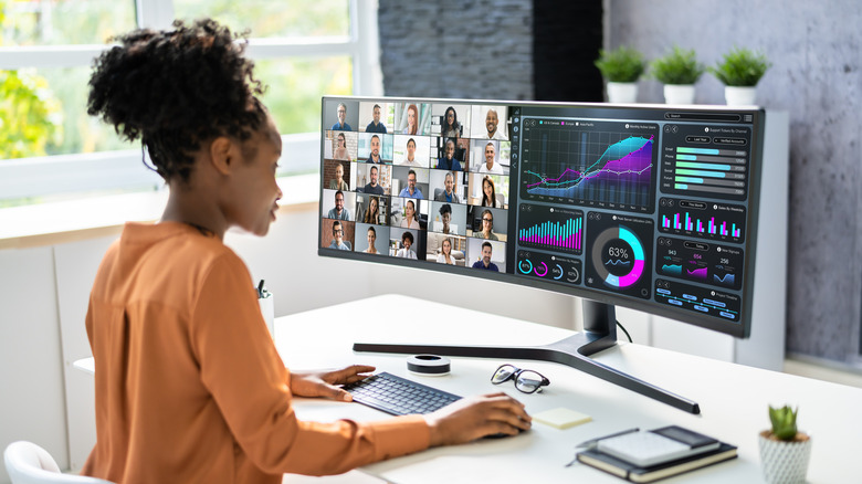 A woman with an ultra-wide monitor on a video call and looking at data at work