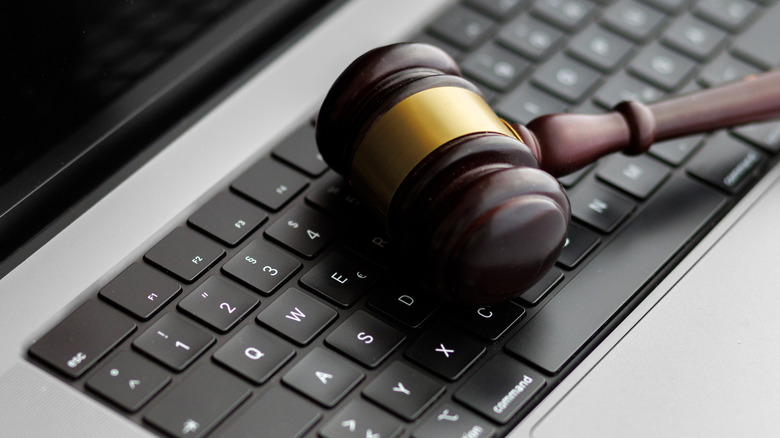 A brown and golden gavel lays across a black keyboard on a silver computer