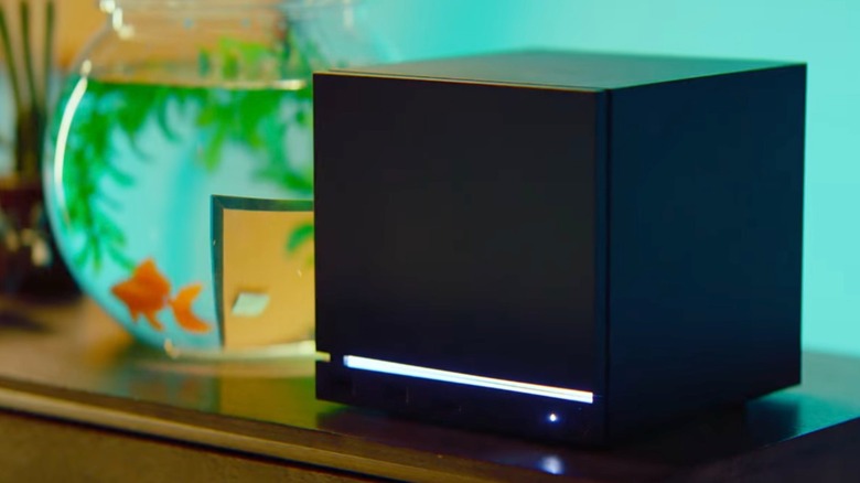 A black Steam Machine by Valve sits on a table next to a fishbowl with an orange goldfish swimming around