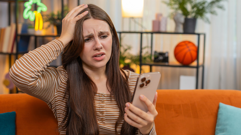 a woman upset looking at her phone in a living room