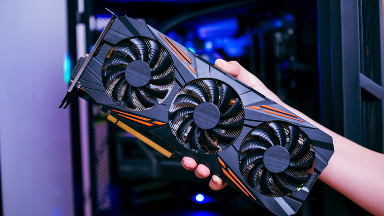 A hand holding a graphics card outside of a gaming PC