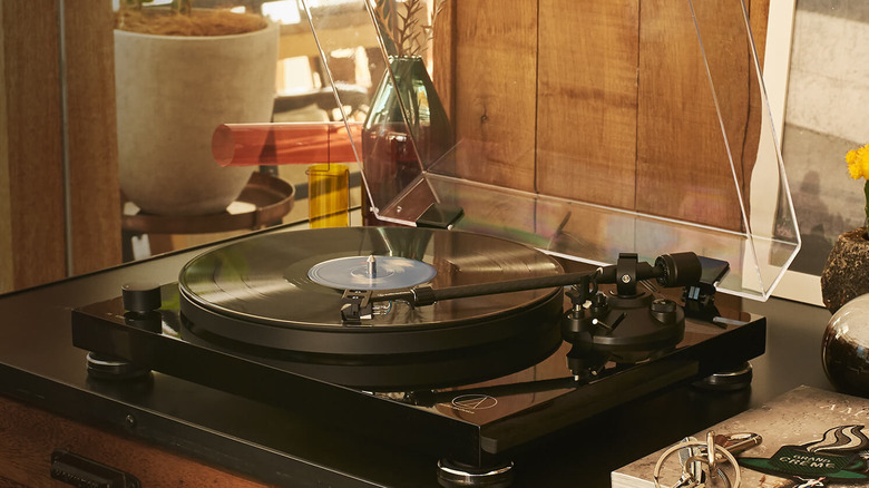 Audio-Technica turntable playing a vinyl record on a wooden cabinet with a dust cover raised