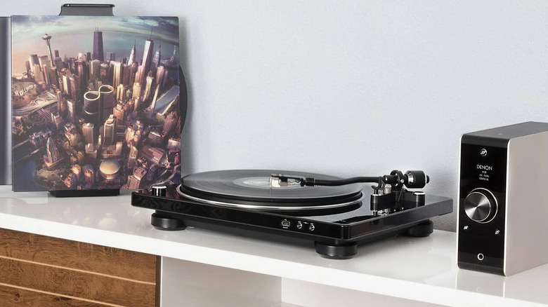 A Denon turntable with a vinyl record on and an album sleeve displayed upright beside it.