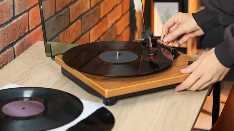 A hand adjusting the tonearm of a record player, with another vinyl record lying on the table in foreground