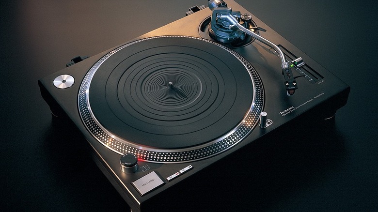 A Technics direct-drive turntable viewed from above, showing the platter, tonearm, and control buttons against a dark background.
