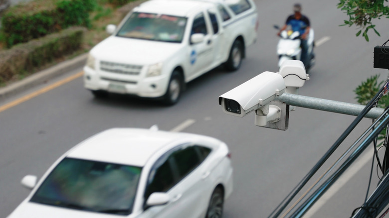 traffic camera on side of busy stress, cars and motorcycle visible in background