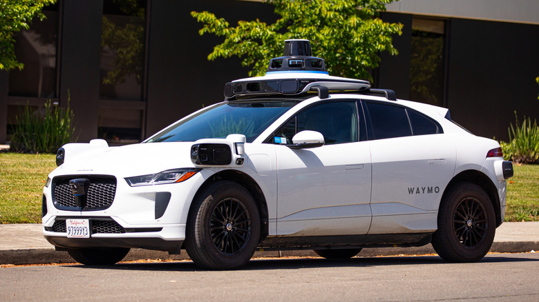 A white Jaguar I-PACE set up with Waymo cameras and sensors parked by the curb