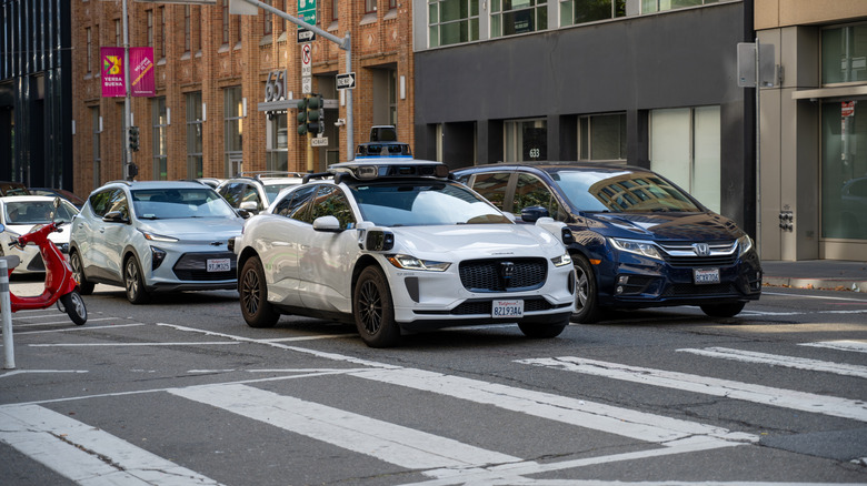 Waymo self-driving taxi in traffic waiting at a light.