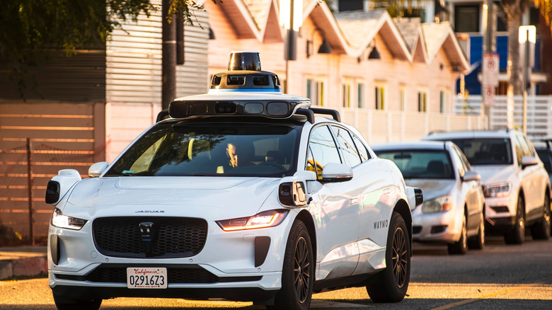 waymo driving on a street, person visible in the backseat