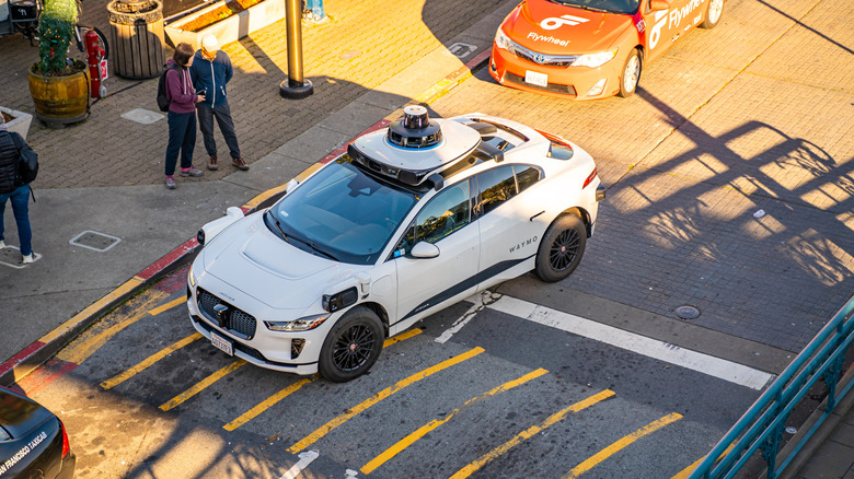 waymo vehicle in a crosswalk, people standing near it