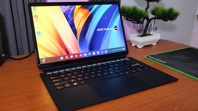 A black ASUS Vivobook OLED laptop on a brown wooden desk displaying a Windows 11 desktop