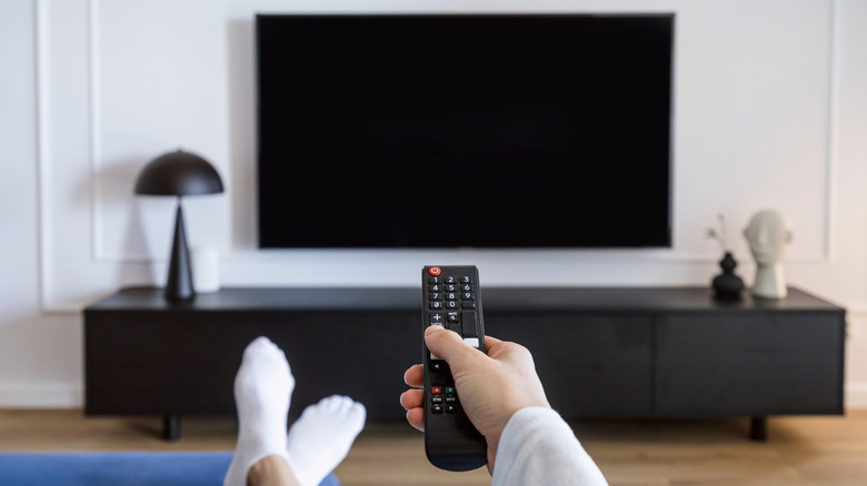 A hand holding a remote up to a black wall-mounted TV panel in a living room