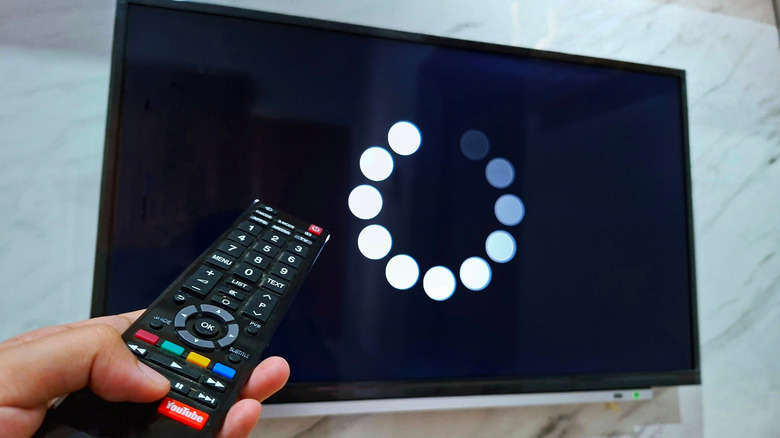 A hand holding a TV remote pointing at a television screen displaying a loading symbol