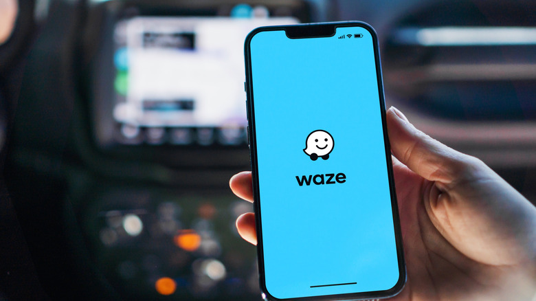 A person holding a phone in a car with the Waze logo on the screen