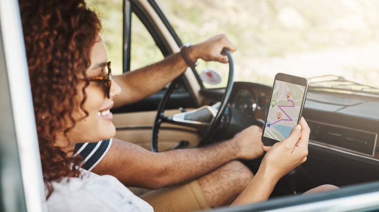 Woman holding phone showing navigation app while in the passenger seat