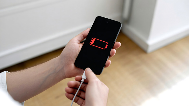 low battery icon on smartphone display as person plugs in a USB charger