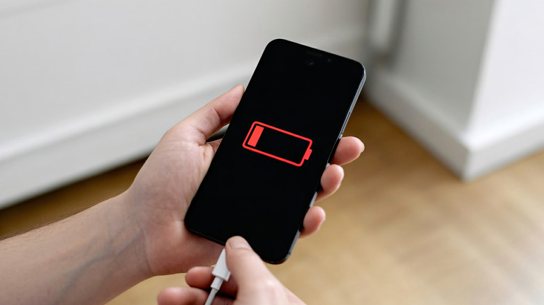 A person holding a phone in their hand displaying a dead battery icon