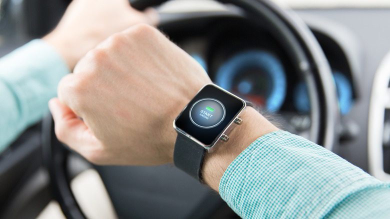 A person inside a car looking at their smartwatch with their other hand on the steering wheel