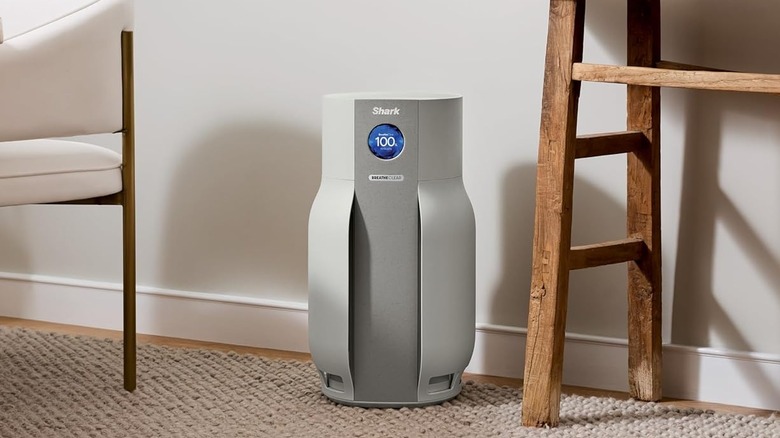 The Shark BreatheClear MAX air purifier on a carpeted floor, between a chair and a table.