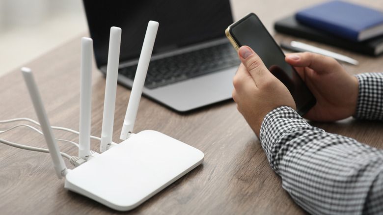 Man using a phone and a laptop near a traditional Wi-Fi router