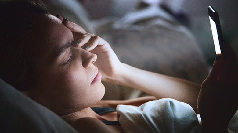 A woman staring at her phone while in bed