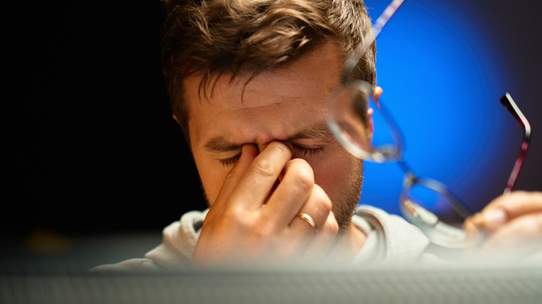 A man taking off his glasses and rubbing eyes while in front of a computer screen