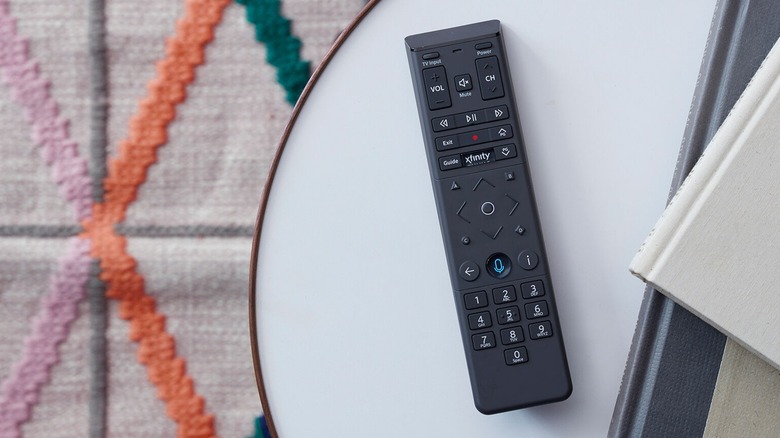 An black Xfinity Voice Remote sitting on a white table next to two books