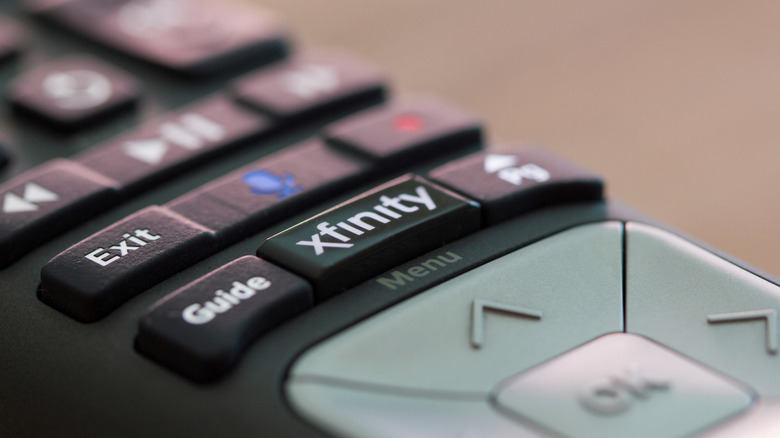 A closeup of the Xfinitiy button on a black television remote, which also has a grey directional pad
