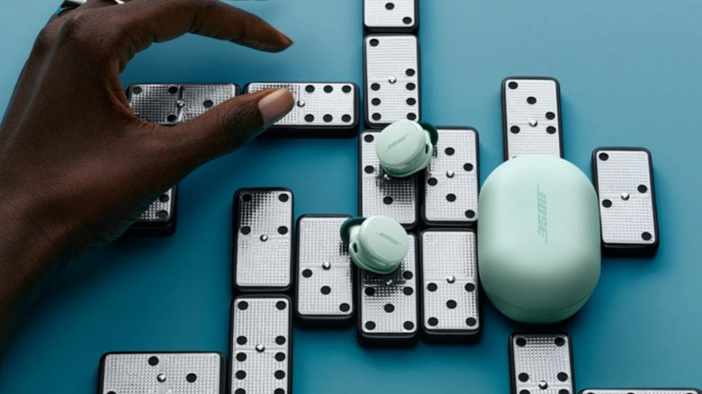 The Bose QuietComfort Earbuds placed on top of dominos, which are set against a blue backdrop.