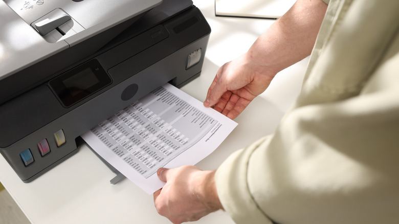 Someone retrieving paper with document printed from a small printer.