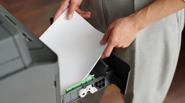 Someone loading blank paper into a printer tray.