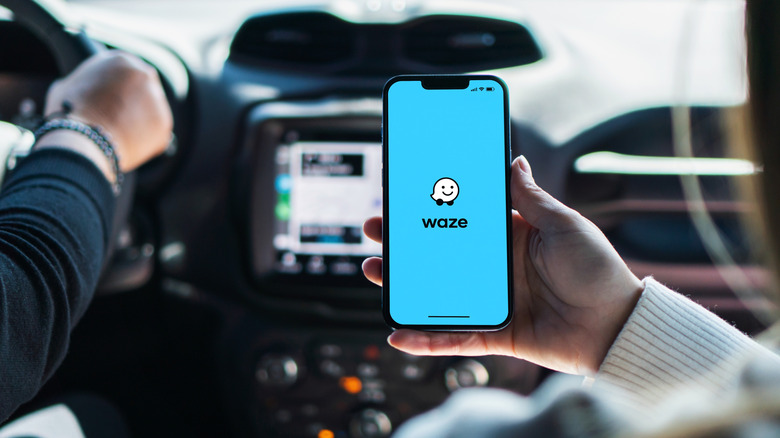 Someone holding a smartphone up inside a car with the Waze intro screen on display.